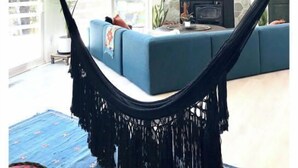 Una hamaca en una habitación luminosa con chimenea de piedra, ventanas amplias y un sofá azul.