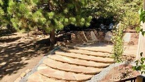Una escalera de piedra conduce a una zona de estar con sillas, rodeada de árboles y un muro de piedra.