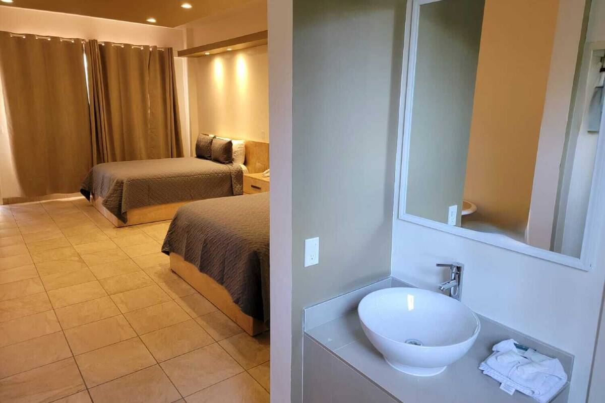 A hotel room with two beds, a bathroom with a large mirror and a white sink.