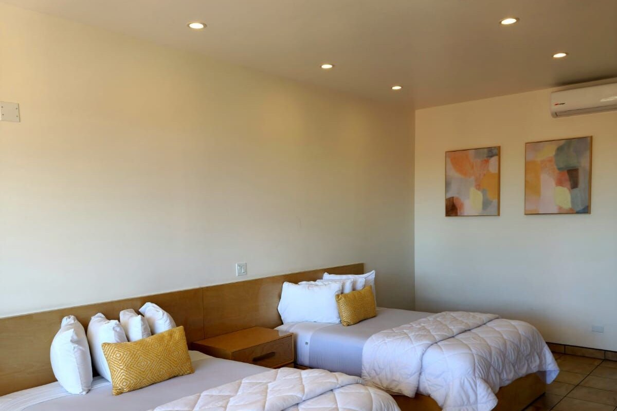 Habitació d'hotel amb dos llits, cadascun amb roba de llit blanca i un edredó acolxat. Hi ha llums al sostre i una unitat de climatització a la paret.