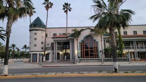 A hotel with a central tower, a large arched window, and palm trees in the foreground. - Hotel Paraíso Las Palmas (Ensenada)