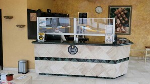 A reception desk with a tiled floor, a clock on the wall, and a framed picture above the desk. - Hotel Paraíso Las Palmas (Ensenada)