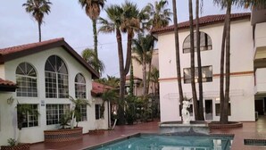A swimming pool with a brick deck, surrounded by palm trees and a building with arched windows. - Hotel Paraíso Las Palmas (Ensenada)