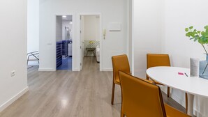 Una stanza moderna e minimalista con un tavolo bianco rotondo e due sedie arancioni. Sul tavolo c'è una piccola pianta e una porta che conduce a un bagno con un lavandino e uno specchio bianchi.