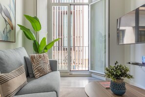 A living room with a grey sofa, a large green plant, and a small table with a book and a decorative pot.