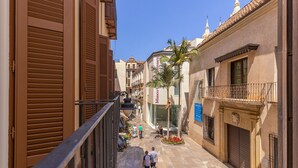Una stretta via fiancheggiata da edifici, con un cielo azzurro limpido e alcuni passanti.