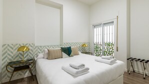 Camera d'albergo con un letto grande, un comodino con una lampada, una finestra vista su del verde e un rastrelliera per stendiabiti.