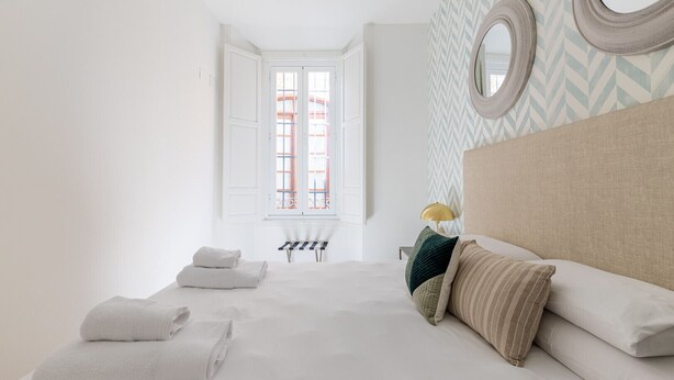 Ein Hotelzimmer mit einem Bett, zwei Handtüchern, einem Kopfteil, einem Fenster und einem Stuhl.