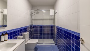 Ein Badezimmer mit weißen Fliesen, einem blauen Duschbereich, einer Toilette und einem Waschbecken mit Toilettenartikeln.