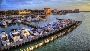 A marina with numerous boats docked at wooden piers, surrounded by buildings and a calm waterfront.