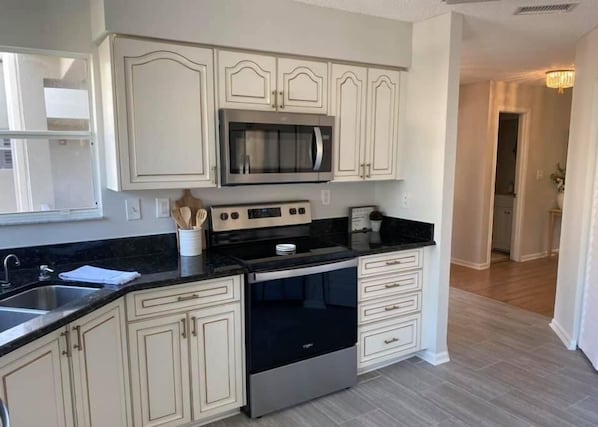 A kitchen with white cabinetry, a stainless steel microwave, oven, and stove. There is a sink with a faucet, and a countertop with a coffee maker and a mug.