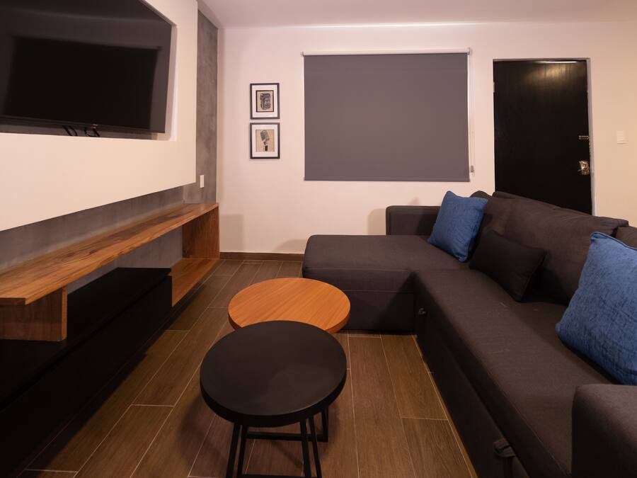 A modern living room with a sectional sofa, a round coffee table, a TV mounted on the wall, and a door.