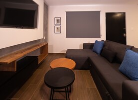 Uma sala de estar moderna com um sofá em formato de L, uma mesa de centro redonda, uma TV fixada na parede e uma porta.