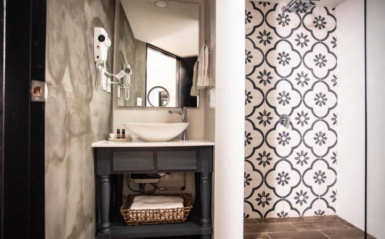 A bathroom with a marble wall, a white sink, a mirror, a hairdryer, and a patterned shower wall.
