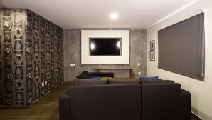 A modern living room with a large flat-screen TV mounted on the wall, a sectional sofa, and a decorative wall with framed pictures. - Casa Bruna Luxury Lofts (Tampico)