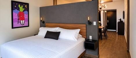 A hotel room with a large bed, a nightstand, a wall-mounted lamp, and a painting.