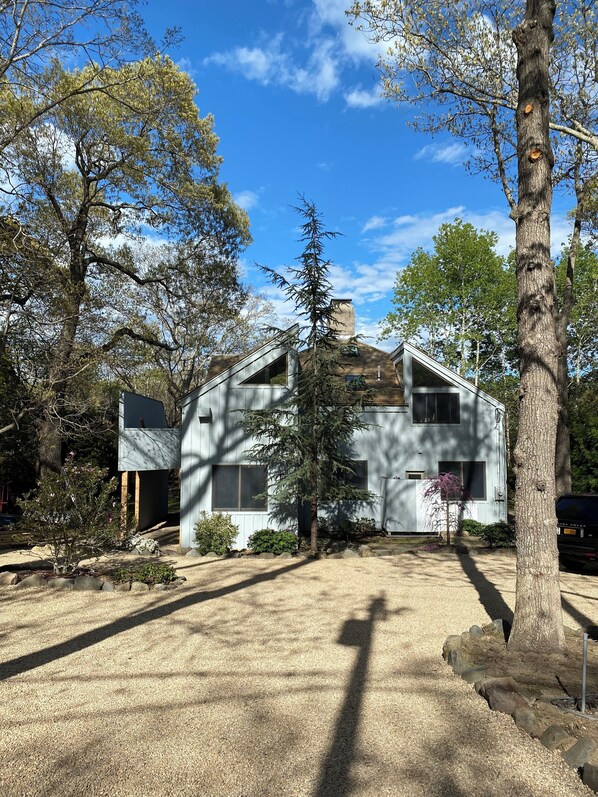 Una casa de dos pisos con techo inclinado, rodeada de árboles y un camino de entrada de grava.