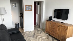 Een woonkamer met een zwarte leren bank, een houten kast, een televisie en een visgraatvloer.