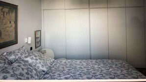Een slaapkamer met een bed, nachtkastje, lamp, een ingelijste foto en een grote garderobe.