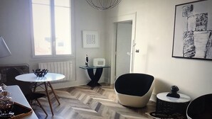 Een moderne woonkamer met een visgraat parketvloer, een ronde glazen tafel, een zwarte fauteuil en een witte bank.