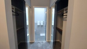 Un couloir étroit, avec des placards de part et d’autre, qui mène à une salle de bain dotée d’une douche et de toilettes visibles à travers une porte en verre.
