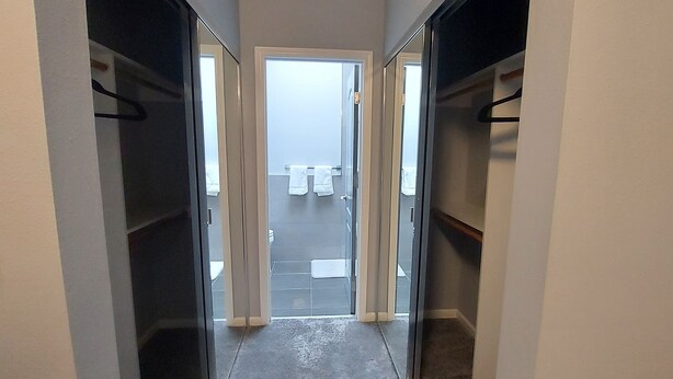 Un couloir étroit, avec des placards de part et d’autre, qui mène à une salle de bain dotée d’une douche et de toilettes visibles à travers une porte en verre.
