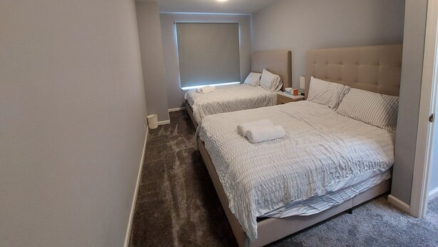 Une chambre avec deux lits, une fenêtre, un luminaire au plafond et un sol recouvert de moquette.