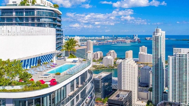 Ett modernt hotell med en pool på taket, utsikt över stadens silhuett och havet.