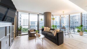 Ett modernt vardagsrum med en soffa, fåtölj, soffbord och matbord. Stora fönster ger utsikt över stadsbilden.