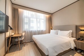 A hotel room with a bed, a desk, a chair, a TV, and a bedside table with a phone. - Hanting Hotel (Kuytun)