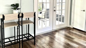 Une pièce avec un plancher en bois, un téléviseur fixé au mur, une plante et un coin bar avec des tabourets.