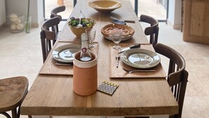 A dining table with a modern pendant light, surrounded by chairs, set with plates, a bowl, and a glass pitcher.