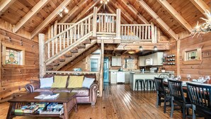 A log cabin interior with a living room, dining area, kitchen, and a staircase leading to an upper level. - Alpine Splendor Cabin Mountain Views Hot Tub (Sevierville)