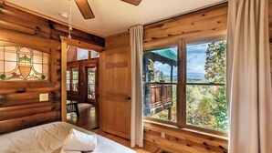 A log cabin room with a bed, a wooden ceiling fan, a large window with curtains, and a view of the outdoors. - Alpine Splendor Cabin Mountain Views Hot Tub (Sevierville)
