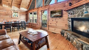 A wooden cabin interior with a dining area, fireplace, and large windows. - Alpine Splendor Cabin Mountain Views Hot Tub (Sevierville)