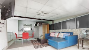 A living room with a blue sofa, red chairs, a dining table, and a kitchen in the background.