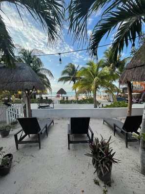 Un patio frente a la playa con sillones, una sombrilla de paja y plantas en macetas.