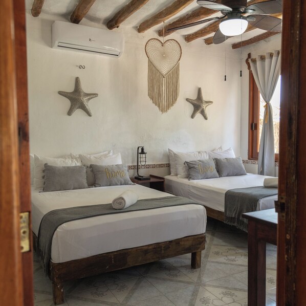 Una habitación con dos camas, ventilador de techo, aire acondicionado y estrellas de mar decorativas en las paredes.
