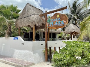 A sign for 'Casa Playa' with a thatched roof structure, surrounded by palm trees and a white wall. - Casa Playa Ocean Front (Isla Holbox)