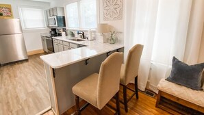 Een moderne keuken met een centraal eiland, een eethoek met twee stoelen, en een bank met kussens.