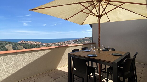 Un patio con mesa y sillas, una sombrilla y vistas a un pueblo costero.