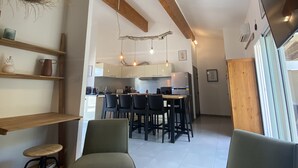 Una cocina moderna con armarios blancos, un comedor con sillas y un televisor montado en la pared.