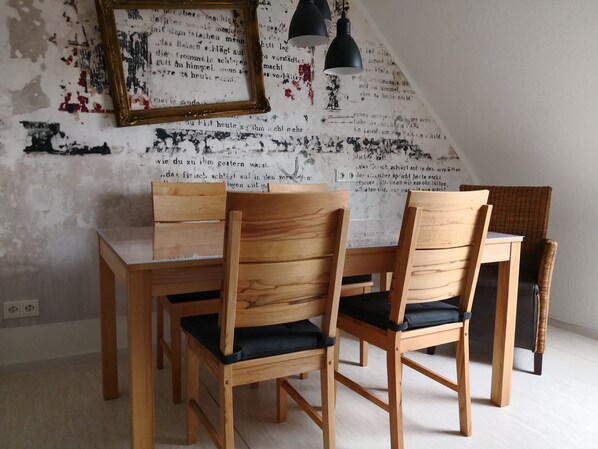 A dining area with a wooden table and chairs, a framed picture, and a wall with a distressed design. - Ferienwohnung Gebauer (Hornbach)