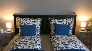 Un lit double avec une couverture bleue, deux tables de chevet avec des lampes et une tête de lit ornée d’un motif cachemire.