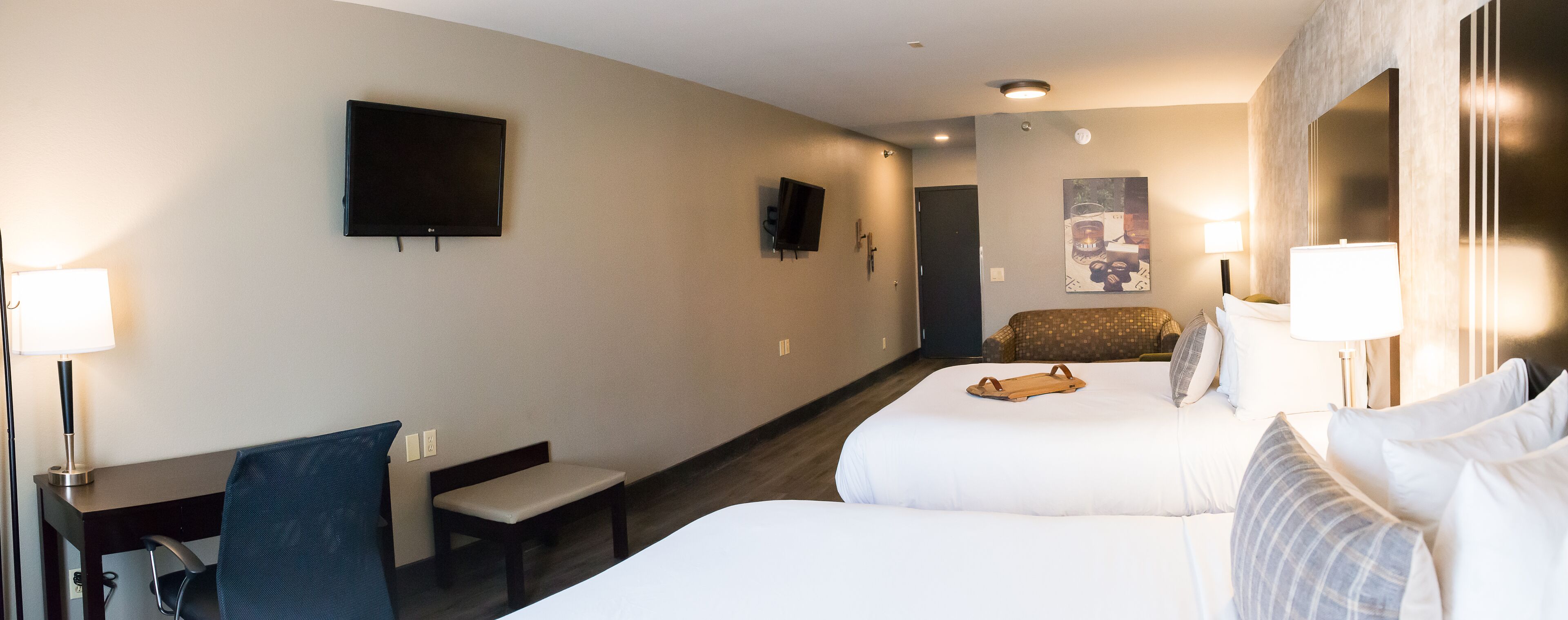 Ein Hotelzimmer mit zwei Betten, einem Schreibtisch, einem Stuhl, einem Fernseher und einem kleinen Tisch mit Tablett.