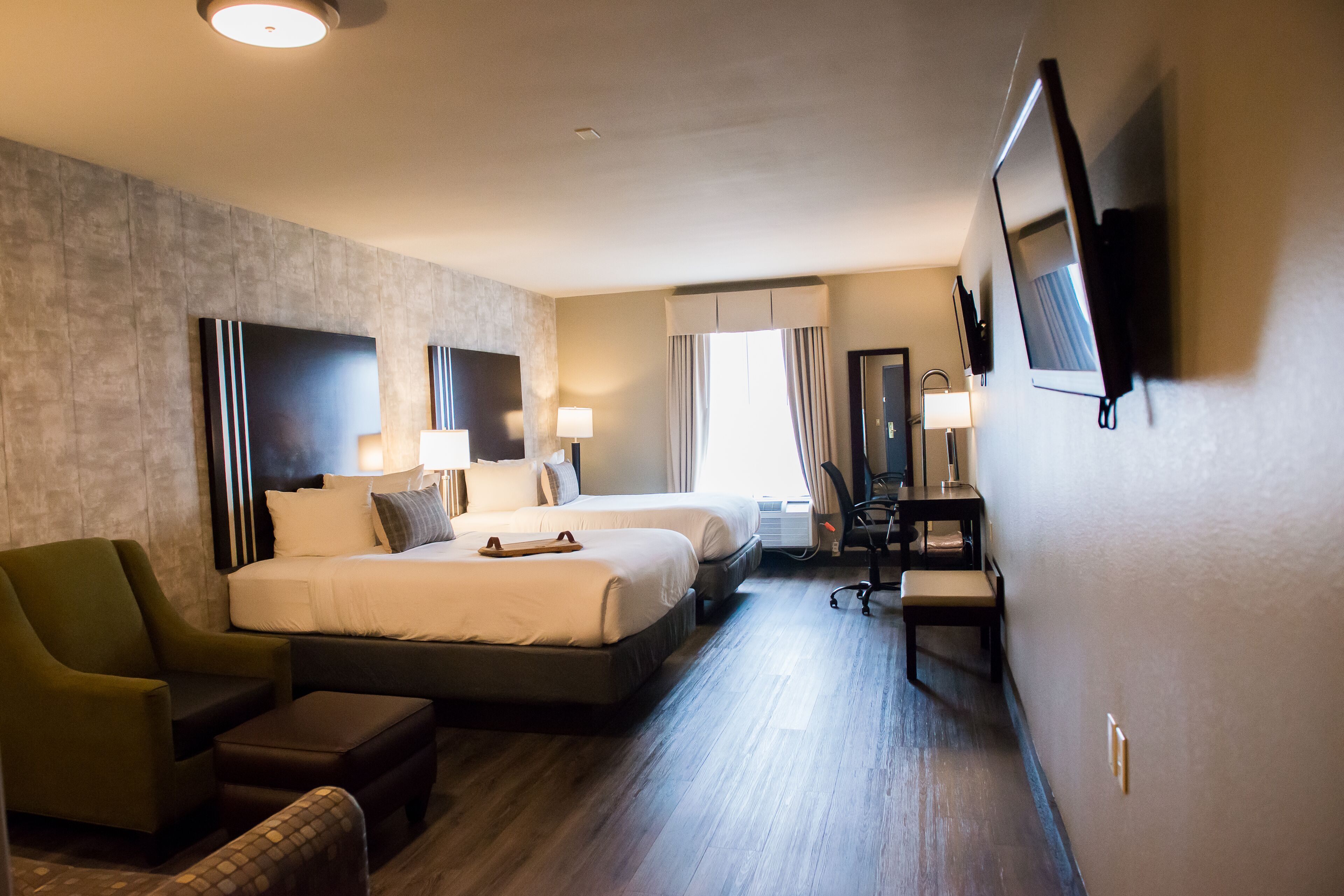 Habitación de hotel con dos camas, un escritorio, una silla y televisión montada en la pared.
