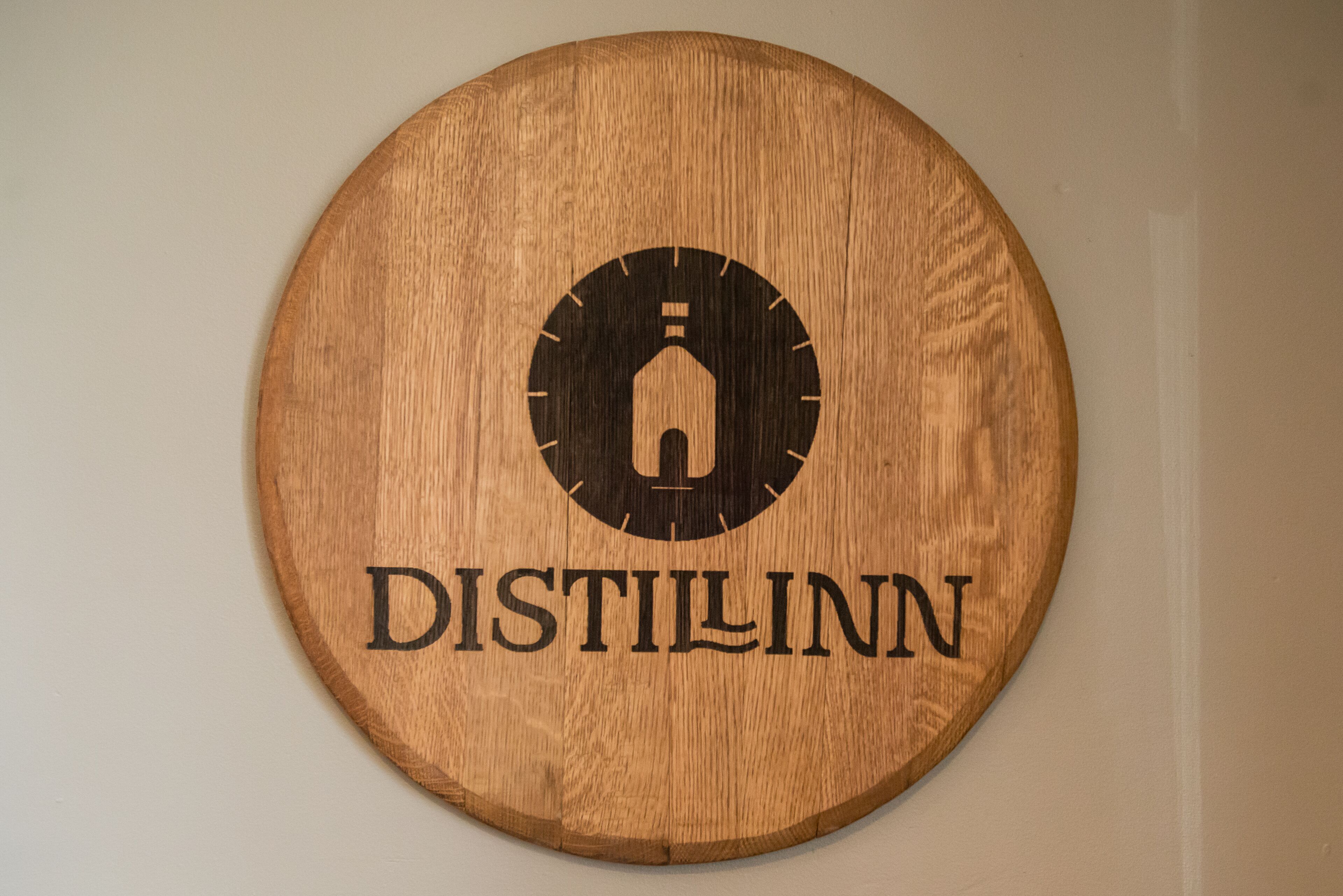Un panneau circulaire en bois, orné d’un logo et du mot « DISTILLINN ».