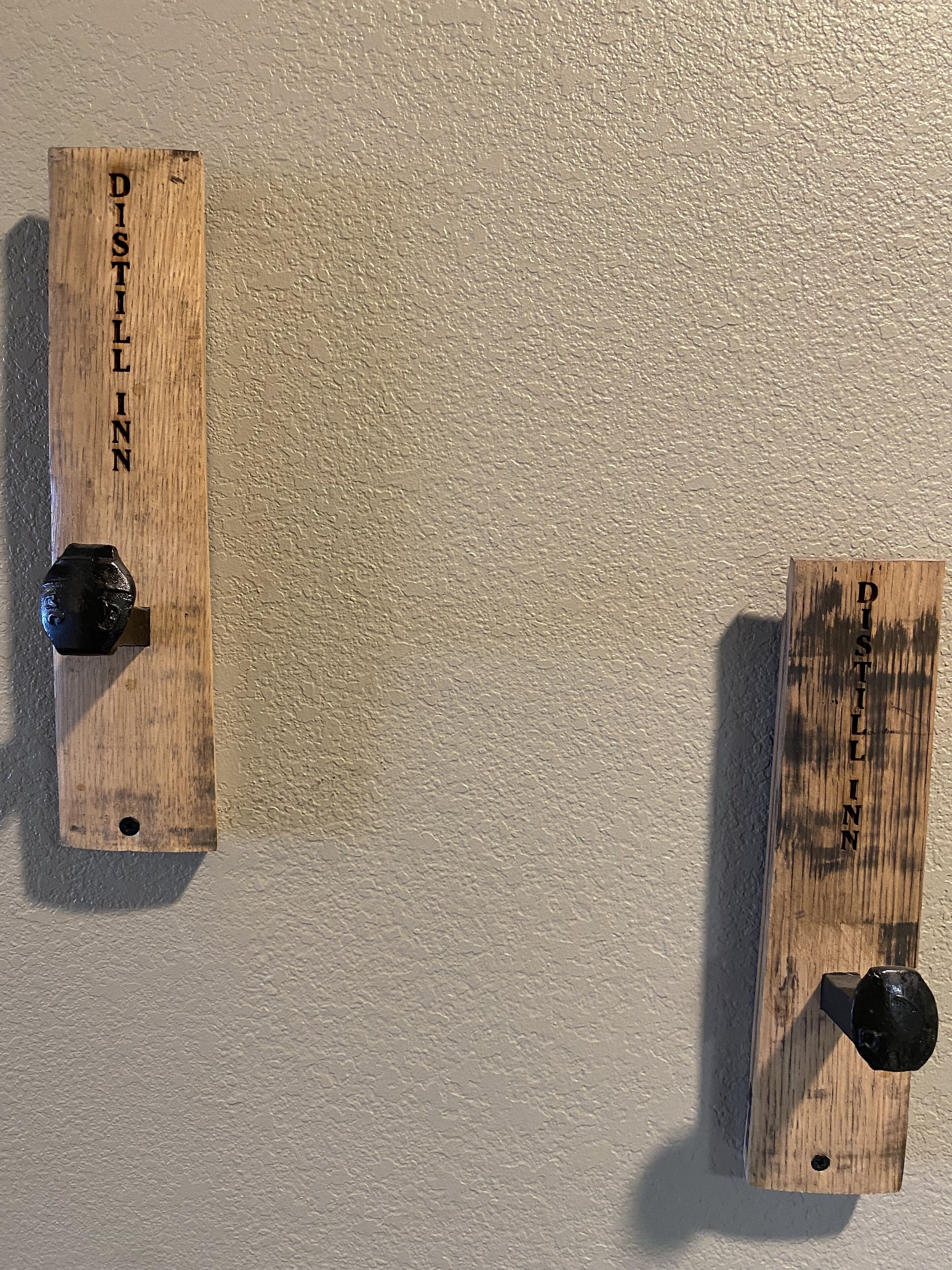 Two wooden wall-mounted objects with black knobs, each labeled 'DISTILL INN.'