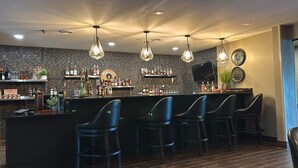 A bar area with a counter, multiple bar stools, and a variety of liquor bottles. - Distill-Inn (Bardstown)
