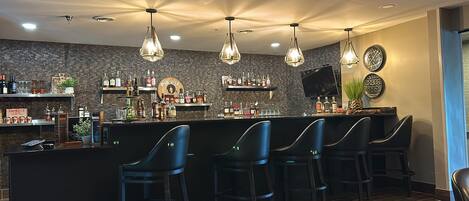 A bar area with a counter, multiple bar stools, and a variety of liquor bottles.